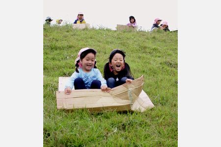 梅雨の晴れ間に堤防で草すべり　成仁幼稚園が段ボール使って